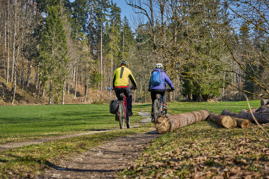 Happy senior couple enjoying an active lifestyle, riding electric bikes on a forest trail in spring. Outdoor recreation, healthy aging, and leisure time in nature on a sunny day.
