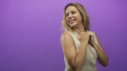Fototapeta premium Woman smiling with fists raised and exposed arms wearing a sleeveless vest in a purple studio; joy empowerment.