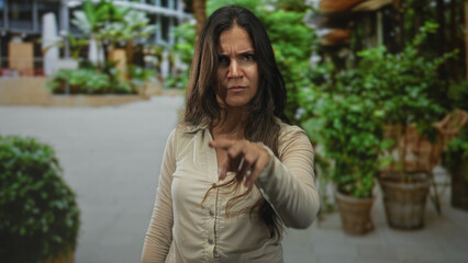 Fototapeta premium Woman with visible face scowling on a street, long brown hair and beige buttoned shirt with tense upright posture; anger defiance.