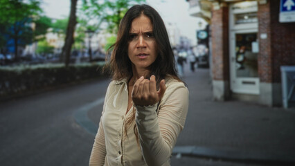 Fototapeta premium Young woman points finger at camera on a busy city street, stern brow, outstretched hand and pursed lips, waist up framing; anger accusation.