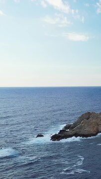 Waves crash against a rugged rocky coastline under a clear sky near Cargese, Corsica. Tranquil seascape with blue water and natural coastal scenery.