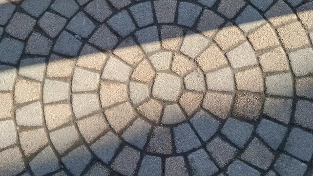 Circular stone paving pattern with natural light shadow play. Textured cobblestones rhythmic geometric design on city walkway or private garden patio area. Decorative pavement in concentric circles
