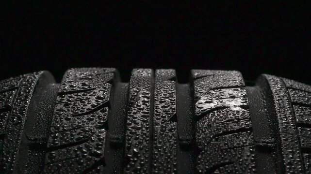 Tire Tread After Rain. Wet tire spinning on a black background close-up. It is covered with sparkling water drops