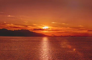 Fototapeta premium Golden Alaskan fjord sunset illuminating calm waters and distant forested mountain silhouettes