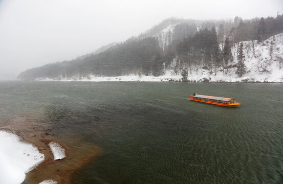 Winter scenery of tourist boats cruising on Mogami-Gawa, one of the three most rapid rivers in Japan, with the riverside hills covered by heavy snow on a cold foggy morning in Yamagata, Tohoku, Japan