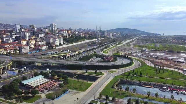 Aerial drone view of a newly constructed multi-level interchange on Maltepe coastal road with light vehicle traffic, residential buildings, green areas and partly cloudy spring sky, Istanbul, Turkey