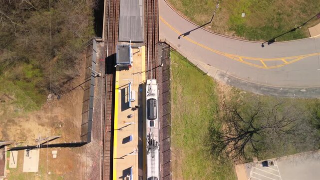 Top down drone view of a train stopped at a station platform beside a curved road