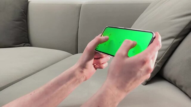 Hands hold smartphone with green screen and perform finger gestures like tapping and playing. Close up view shows chroma display with interaction. Concept mobile gaming, app testing, digital