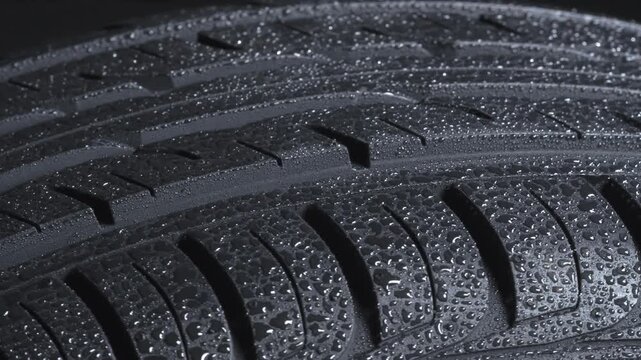 Sparkling Drops on a Car Tire. Wet tire spinning on a black background close-up. It is covered with sparkling water drops