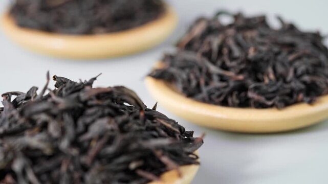 Macro Close-up of Premium Dried Black Tea Leaves on Wooden Plates, Light Gray Background for Tea Culture
