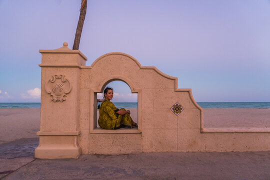 A woman sits in a window of a building overlooking the ocean