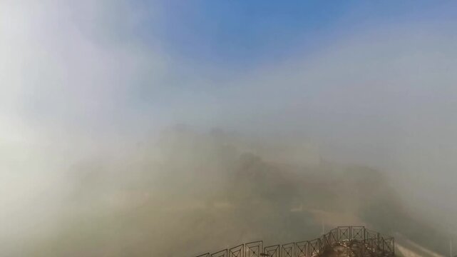 Misty view of Lombardy Castle emerging from clouds in Enna, Sicily, Italy, showcasing the gradual reveal of the historic structure against a blue sky