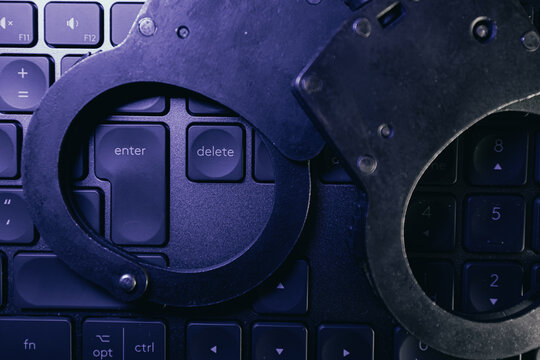 Handcuffs resting on a black computer keyboard with highlighted keys for enter and delete, creating a contrast between technology and law enforcement