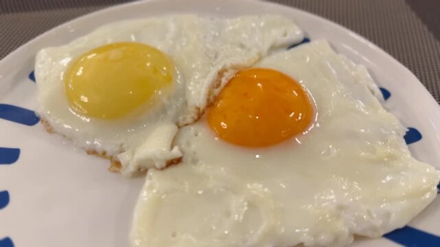 Fried eggs with bright yolks on a white plate with blue stripes