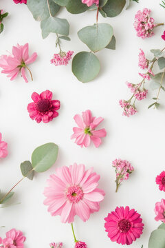 Fresh pink flowers and eucalyptus leaves arranged on a white surface vertical frame
