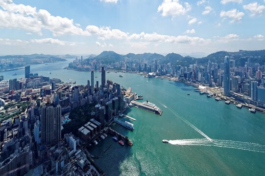 Aerial panorama of Hong Kong and  Kowloon with a city skyline of crowded skyscrapers by Victoria Harbour and ships sailing between Tsim Sha Tsui and Central Ferry Piers on a sunny day