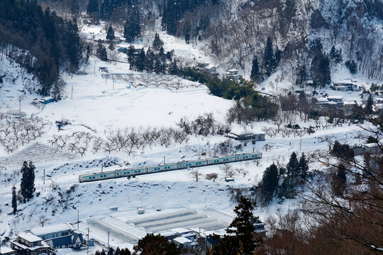 Aerial view from Risshaku-ji Buddhist Temple on the mountainside overlooking Yamadera village and a train of JR Senzan Railway traveling through the valley in snowy winter season in Yamagata, Japan