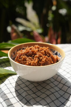 Close-up of traditional Indonesian dry shredded beef rendang or spiced roasted grated coconut, served in a bowl under natural sunlight.