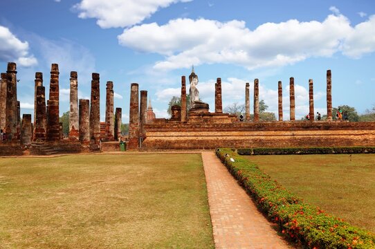 View of a Buddha statue seated among decadent columns of a ruined shrine in Wat Mahathat, an ancient Buddhist Temple and a beautiful UNESCO heritage site in Sukhothai Historical Park in Thailand, Asia