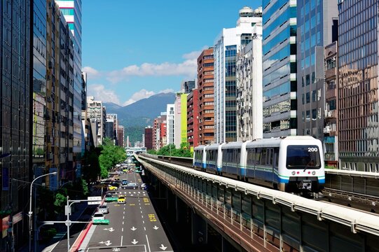 A metro train traveling on the elevated rail of Taipei MRT between office towers under blue sky ~ View of a public transportation system in Taipei, the capital city of Taiwan, on a beautiful sunny day