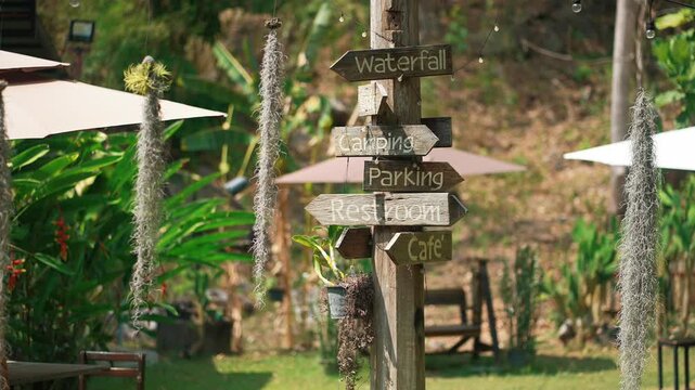 Wooden signpost with directional arrows in green park setting with travel destinations, Rustic outdoor guide with directions to waterfall camping cafe and facilities in natural landscape