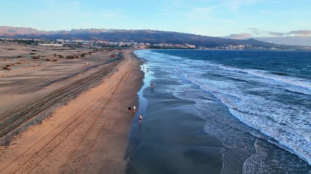 Drone flight along beach shoreline with gentle waves and walking people, LUT, 60 fps