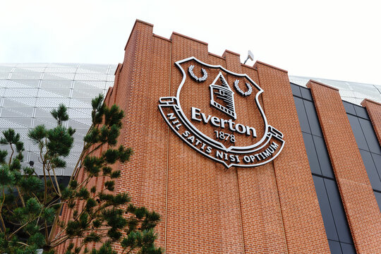 Everton Football Club emblem on a brick stadium wall under cloudy skies.