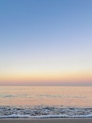 Fototapeta premium White sea foam against a pastel sunset sky. Vertical seascape background.