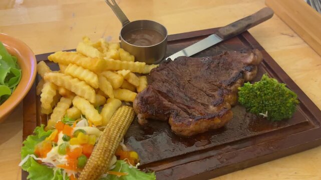 Close up on juicy grilled picanha steak served with crispy fries, small salad, vegetables, and sauce on a wooden board