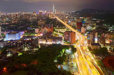 Fototapeta premium Aerial view over the interchange of Shuiyuan Expressway, Keelung Road & Fuhe Bridge in Taipei, with landmark 101 Tower standing amid crowded buildings in Xinyi District & city lights dazzling at night