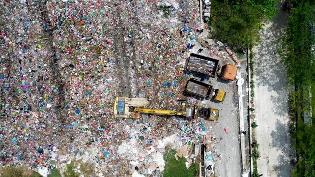 Aerial view of landfill site with excavator and trucks handling large scale garbage waste and pollution
