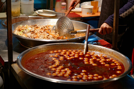 A street vendor cooking in a steaming hot pot the spicy fish balls in chilli stock, one of Taiwanese people's favorite street foods, in a market stall in Taipei, Taiwan