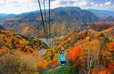 Fototapeta premium A breathtaking view from a cable car of Kurodake Ropeway flying over colorful autumn forests on the mountainside in Sounkyo Gorge in Daisetsuzan National Park, in Kamikawa, Hokkaido Japan