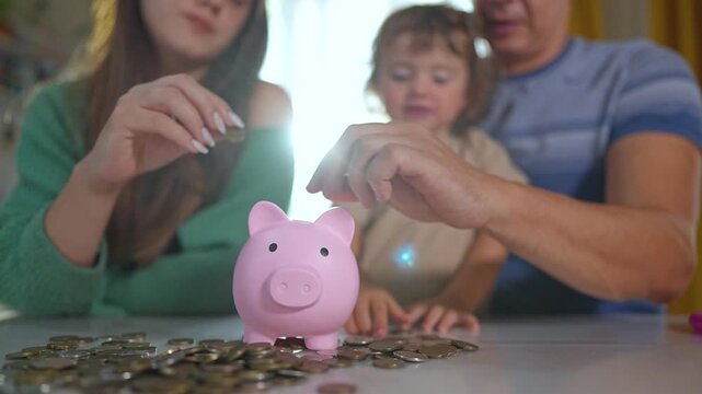 Young family saving money together. Parents and child putting coins into piggybank. Teaching child importance of saving. Piggybank symbolizes child future. Family working together for savings goal.