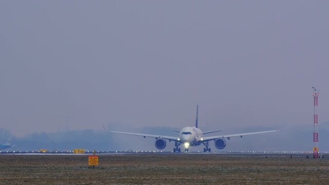 A modern wide-body passenger jet accelerates down the runway and takes off. The video captures the powerful moment of liftoff on a hazy day, ending with a view of the airport terminal.