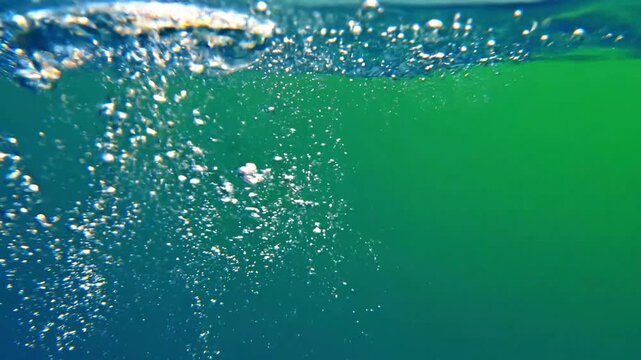 A large, iridescent air bubble ascends gracefully through deep blue-green water, releasing a trail of smaller effervescent bubbles against a gradient background.