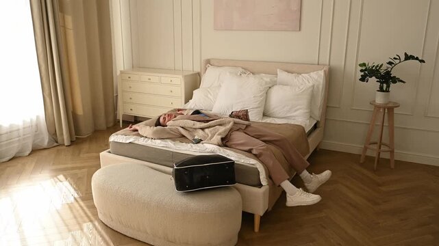 Exhausted woman returning home from a business trip, dropping her travel bag and collapsing onto the bed fully clothed from fatigue and burnout after a long journey or hard day at work