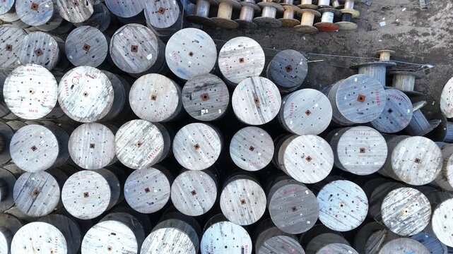 Aerial view of wooden cable spools arranged in a grid pattern on the ground, showcasing the varying sizes and orientations of the spools in a storage area