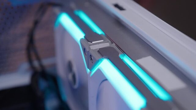 Close-up of professional technician connecting daisy chained fans, preparing to install cooling system on modern high performance graphics card into motherboard slot with rgb lights, slow motion.