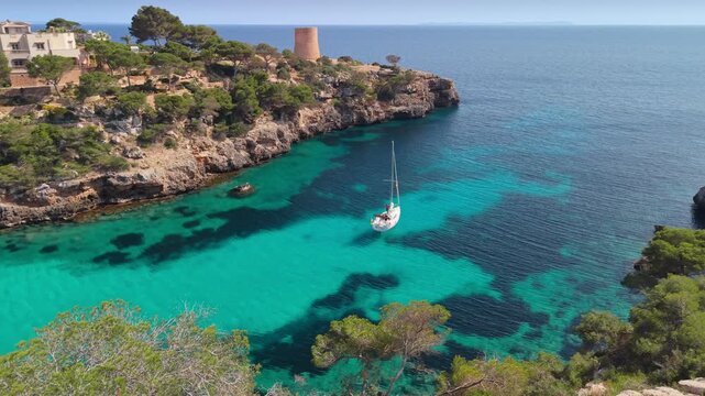 Turquoise water of Cala Pi bay with a white yacht, aerial view of the rocky coast and ancient tower in Mallorca. Paradise bay of Cala Pi with a sailing boat, Mallorca