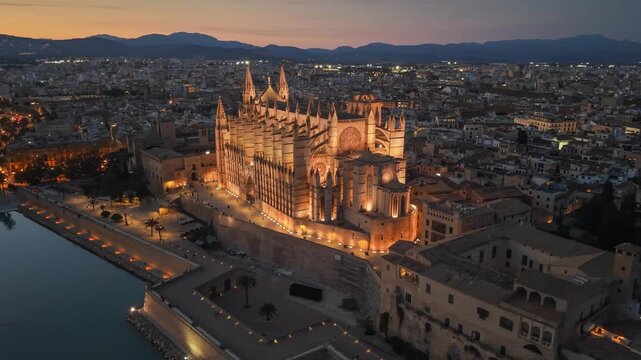 Evening view of the illuminated Cathedral of Santa Maria in Palma, Mallorca aerial footage of the city lights and harbor at dusk. Majestic Palma Cathedral in Mallorca glowing in the evening darkness