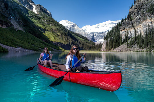 Two smiling young women kayaking in Lake Louise on a summer day, Banff National Park, Alberta, Canada