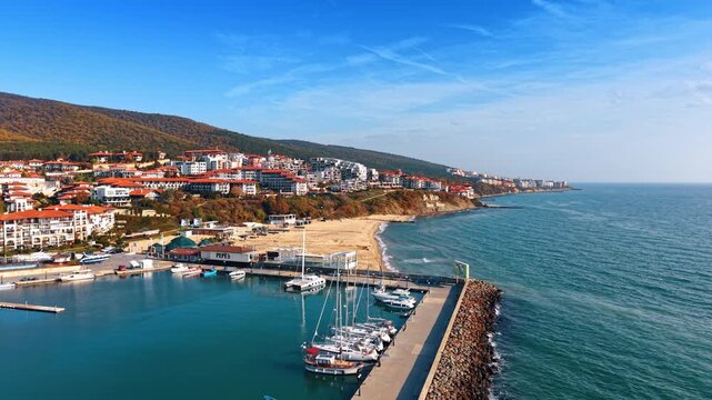 Flying over the pier with some boats standing by. Multiple villas are located on the rocky slopes of Sveti Vlas, Bulgaria.