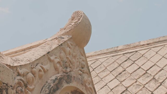A low-angle view highlighting the intricate stone carvings and traditional gabled roof of a historic Southeast Asian temple against a clear, soft blue sky in daylight.