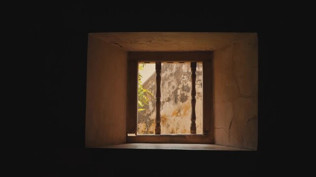 Golden sunbeams illuminate the textured interior of a rustic stone wall seen through a vintage window frame with vertical iron bars, evoking a calm and nostalgic atmosphere.
