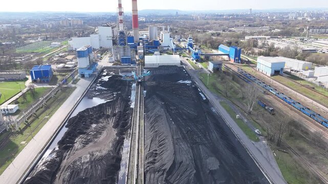 Aerial view of industrial enterprise showing continuous operation of machinery on a coal storage site with surrounding buildings, roads, and rail tracks in a bustling urban landscape