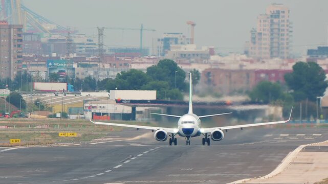 Front view of a colorful passenger jet airplane accelerating down a runway and taking off. The aircraft flies directly overhead against a hazy city skyline. Powerful takeoff with heat haze.