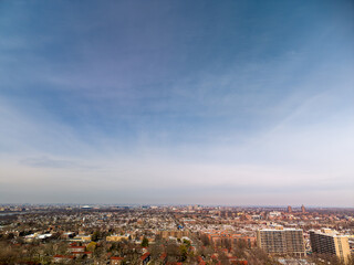 Obraz premium Expansive urban vista showcasing a sprawling residential cityscape with a mix of multistory apartment buildings and individual houses under a wide. Pale blue sky