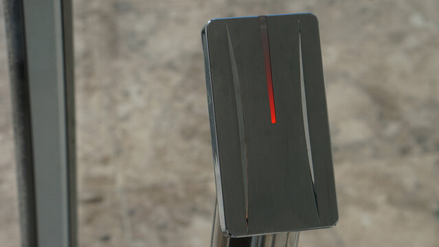 Authentic photo of modern electronic RFID access control reader on metal stand. Contactless key card and bracelet sensor at glass door entrance. Smart hotel security system and touchless technology co