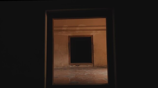 A moody, atmospheric perspective looking through a doorway into a series of dark, connected rooms with terracotta flooring and rustic walls, evoking a sense of mystery and depth.